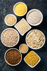 Selection of whole grains in white bowls - rice, oats, buckwheat, bulgur, porridge, barley, quinoa, amaranth on dark background