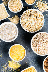 Selection of whole grains in white bowls - rice, oats, buckwheat, bulgur, porridge, barley, quinoa, amaranth on dark background