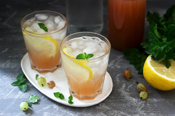 Gooseberry lemonade with mint and ice, a bottle of water and a bottle of gooseberry syrup on a concrete surface.
