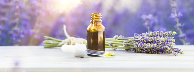 Essential lavender oil in the bottle with dropper on the gray wooden desk. Horizontal close-up.