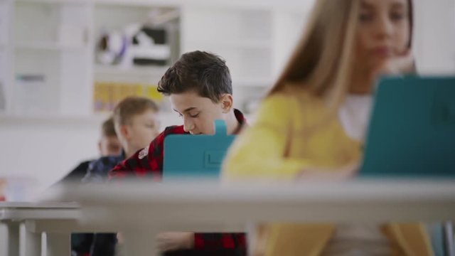 Teen student tries to cheat during a computer science test sitting with laptp by desk in the classroom.
