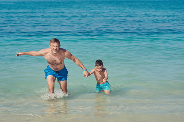 European dad and son having fun on seacoast. They are holding hands and getting out from water.