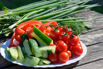 Fresh vegetables and greenery on a wooden background outdoors.