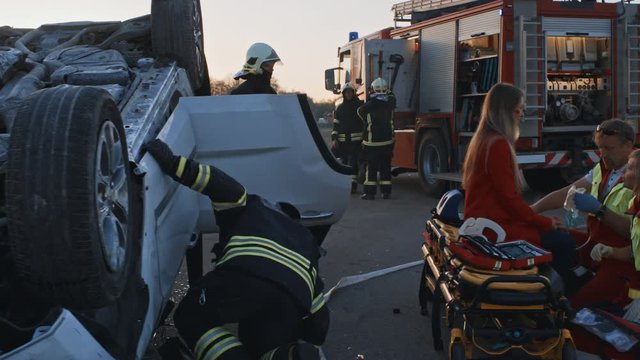 Car Crash Traffic Accident: Paramedics and Firefighters Rescue Injured Trapped Victims. Medics give First Aid to a Female Passenger. Firemen Use Hydraulic Cutters Spreader to Open Vehicle