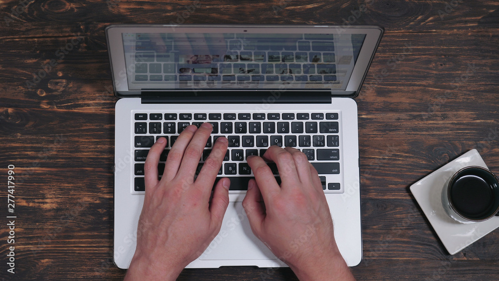 Poster unrtop view male hands typing on computer. working place with wooden desk cup with coffee and laptop