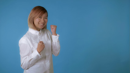 portrait young asian female posing happy dancing on blue background in studio. attractive korean woman with blond hair wearing white casual shirt looking at the camera.