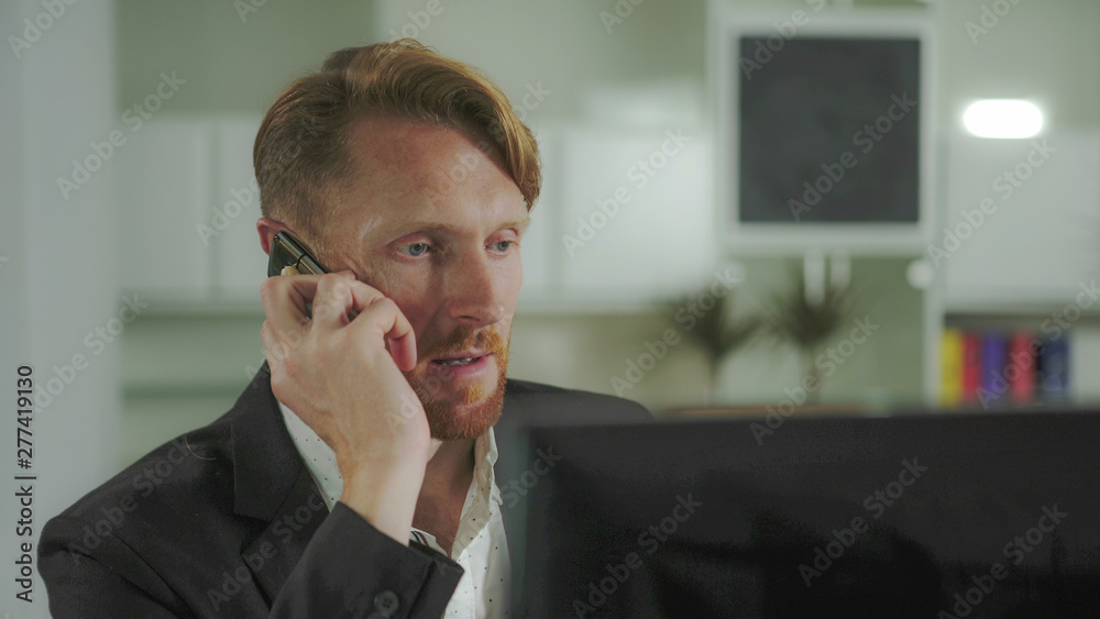 Poster Red-haired man sitting at a computer and calling on the phone. UHD