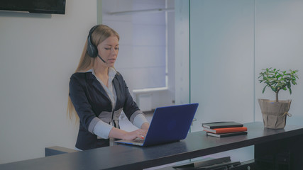 Young professional woman receptionist standing at reception desk talking with client check...