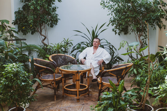 Man In A White Robe Is Resting In A Spa Center Surrounded By Green Plants