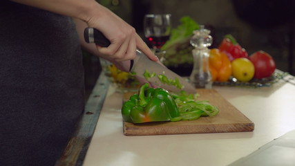 woman hands cutting vegetables closeup details. Female cooking dinner or lunch cut pepper. On the cook table wineglass. Lady holding big knife. Invisible female on the kitchen.