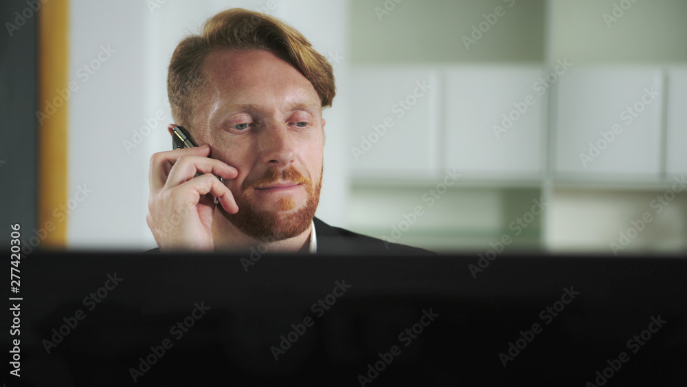 Aufkleber red-haired man sitting at a computer and calling on the phone. uhd