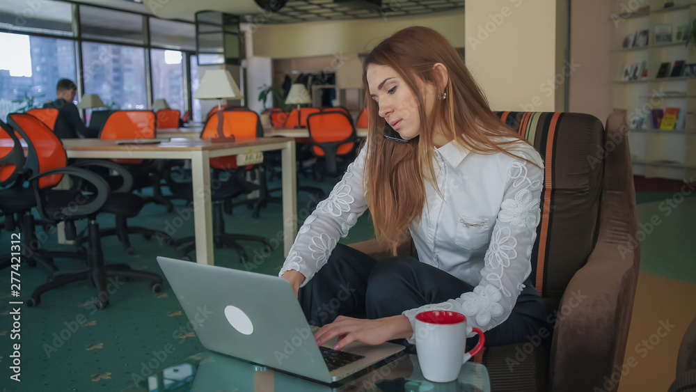 Aufkleber woman working at the big office with panoramic windows . she speaking on the phone and typing on lap