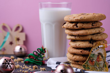 American chocolate cookies, a glass of milk and Christmas decorations. Dark wooden table and pink background. Cookies for the New Year.
