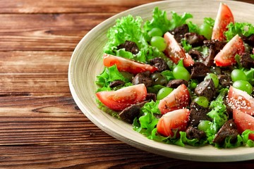 warm salad with chicken liver and grapes on a wooden table
