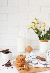 Morning breakfast with hot ground coffee with cinnamon, sweet pastry with chocolate, a bottle of fresh milk and a bouquet of beautiful flowers in a vase against a white brick wall with space for text