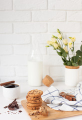 Fototapeta na wymiar Morning breakfast with hot ground coffee with cinnamon, sweet pastry with chocolate, a bottle of fresh milk and a bouquet of beautiful flowers in a vase against a white brick wall with space for text