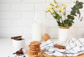 Morning breakfast with hot coffee with cinnamon, delicious cookies with chocolate, a bottle of fresh milk and a bouquet of flowers against a white brick wall with space for text