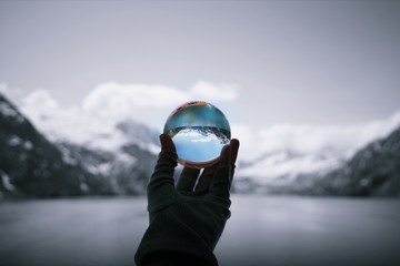 Snow capped mountains in Glacier Bay National Park and Preserve, reflected in crystal ball held by and and