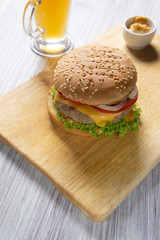 Burger with beef patty, salad, a slice of tomato and cheese, onions and sauce with paprika in a grilled bun with sesame