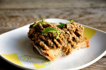 Chicken liver pate sandwich in a white plate on a wooden table.