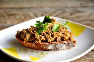 Chicken liver pate sandwich in a white plate on a wooden table.