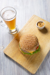 Burger with beef patty, salad, a slice of tomato and cheese, onions and sauce with paprika in a grilled bun with sesame