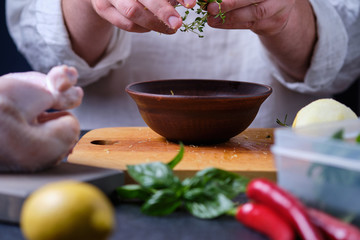 Man puts thyme in a plate. The process of cooking chicken with herbs, spices and lemon in the oven. On the table are the products that are needed for cooking. The hands of the cook in the frame.