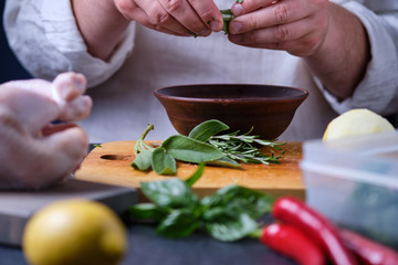 The man puts sage in a plate. The process of cooking chicken with herbs, spices and lemon in the oven. On the table are the products that are needed for cooking. The hands of the cook in the frame.