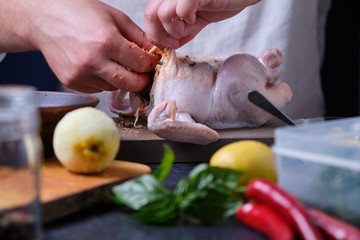 A man rubs chicken with a mixture of pepper, lemon and herbs. The process of cooking chicken in the oven. On the table are the products that are needed for cooking. The hands of the cook in the frame.