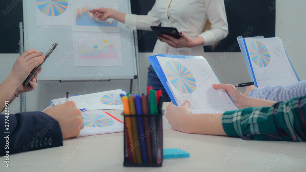 Poster Closeup business team sitting around desk in boardroom. People holding paper report with financial data. Women and men make notes in documents with different colored graphs and diagrams. Speaker