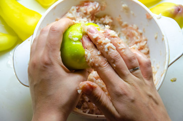 stuffed peppers in the cooking process on a white plate with hands, minced meat with rice and white saucepan