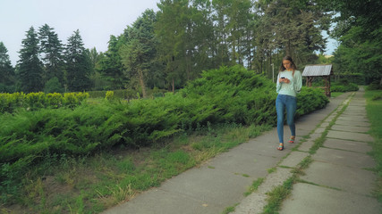 Slender girl in a green blouse is on track in the park, gaining a message on your mobile phone and glances to the side.