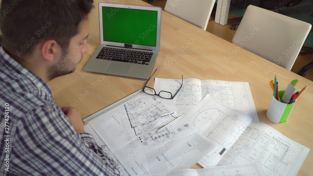 Poster man designer working with blueprint at the working place. on the desk laptop with green screen. male