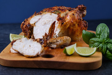 Sliced pieces of oven baked chicken with spices, herbs and lemon on a wooden board with a beautiful ruddy crust.