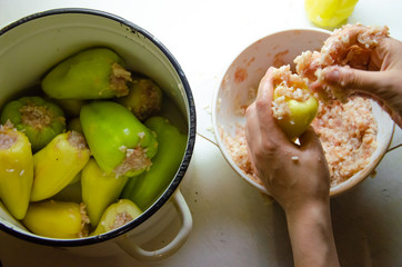 stuffed peppers in the cooking process on a white plate with hands, minced meat with rice and white saucepan