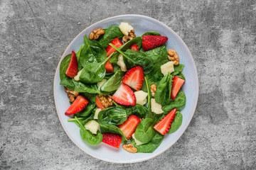 salad with strawberry, spinach leaves, parmesan cheese and walnuts on concrete background. healthy diet food