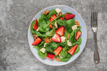 Fototapeta na wymiar Fresh strawberry salad with spinach leaves, parmesan cheese and walnuts with fork. healthy keto diet food