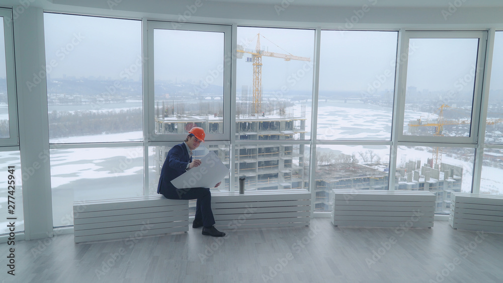 Aufkleber happy building engineer sitting in the modern office looking on the blue print documents with archit