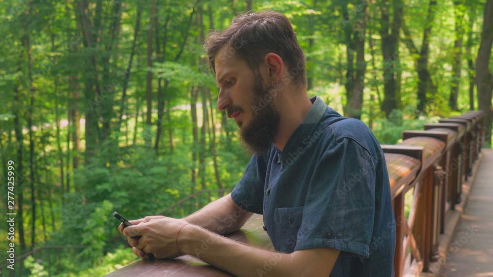 Poster a young bearded guy is holding a smarthone and laughing. he is texting a message or searching intern