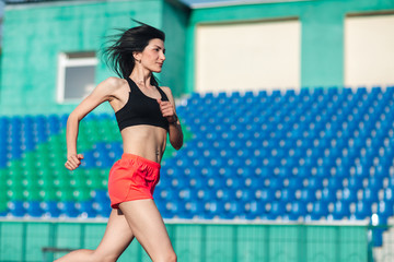 Girl running track on stadium. Real side view of young brunette woman in pink shorts and tank top and pink sneakers. Outdoors, sport