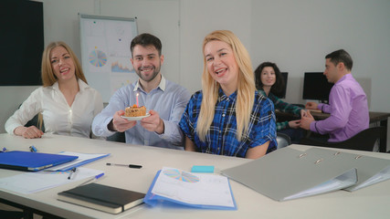 Obraz premium portrait three co workers sitting at the table posing looking at the camera. On the background staff talking with happy smile.