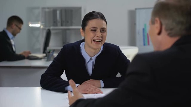 Young female manager insincerely laughing from boss jokes, promotion desire