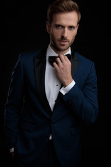 Confident looking groom arranging his black bowtie