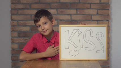Caucasian little boy holding tablet with handwriting word kiss.