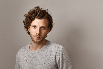 Fototapeta na wymiar Masculine beauty, style and fashion concept. Fashionable 25 year old hipster guy with stubble and blue eyes posing isolated against copyspace wall background, wearing stylish knitted sweater