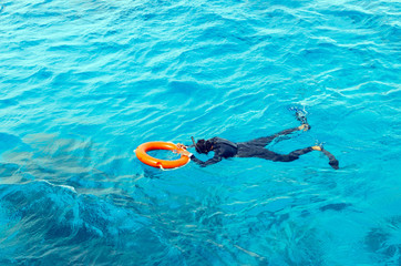 A young man in a diving suit and flippers swims in the sea holding the lifebuoy