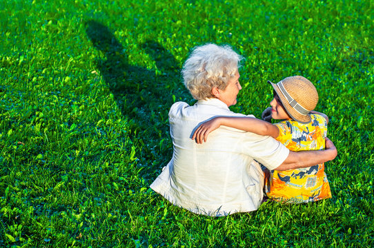 Grandmother and grandson are talking while sitting on the lawn in an embrace. Family relationships, support, friendship, love