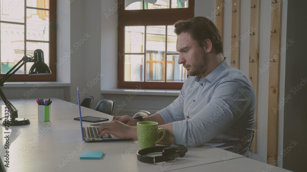 Poster portrait man computing in office. handsome caucasian worker sitting at the desk with table-lamp focu