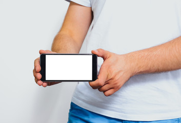 Phone in hand with a blank screen. A man wearing a white T-shirt is holding a phone with a blank display. Content completion concept.
