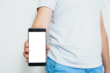 Phone in hand with a blank screen. A man wearing a white T-shirt is holding a phone with a blank display. Content completion concept.